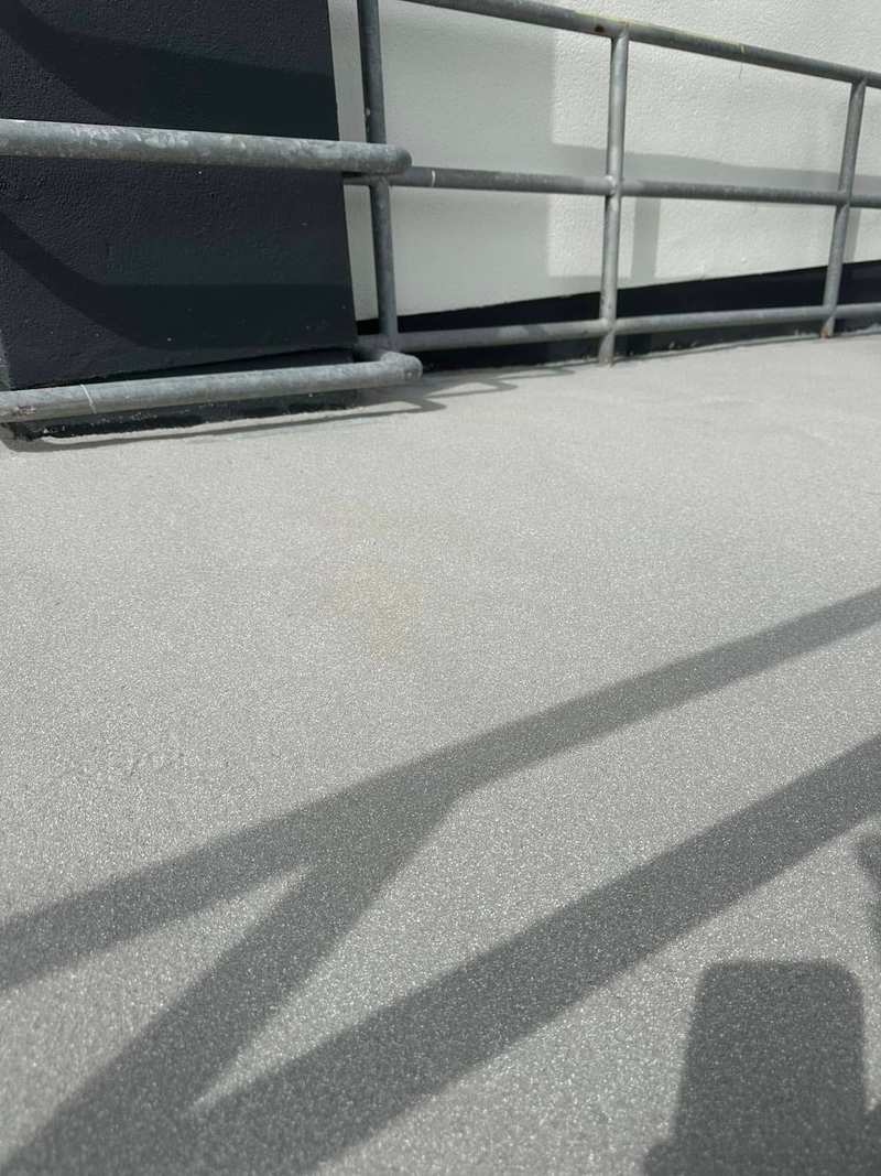 Close view of a grey anti-slip resin surface on an access ramp, with handrail shadows across it