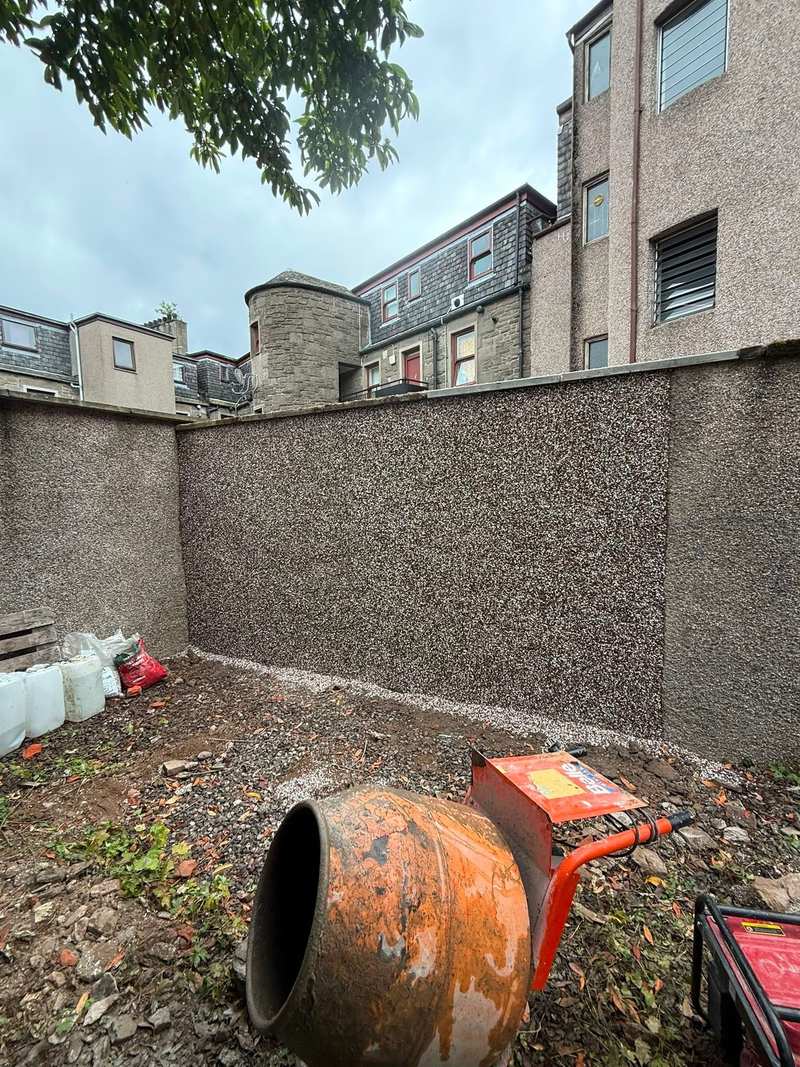 Wide view of a rendered boundary wall in new dry dash roughcast, with a cement mixer in the foreground