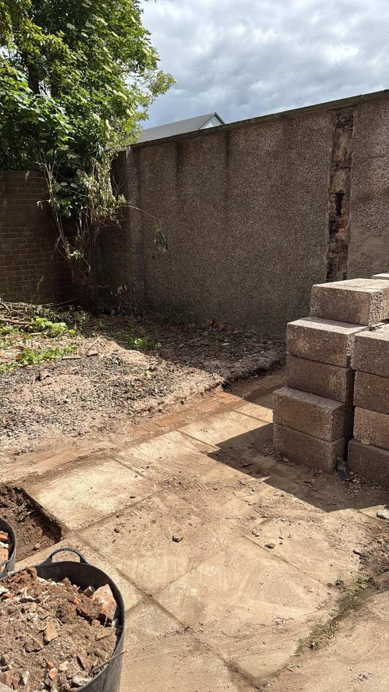 Roughcast boundary wall with a failed vertical section of render and concrete blocks stacked in front