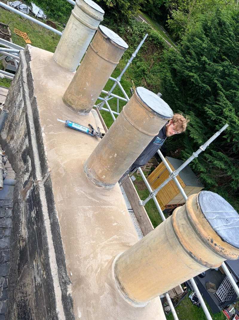 Resurfaced chimney crown around four clay chimney pots on a stone stack, seen from the scaffold above