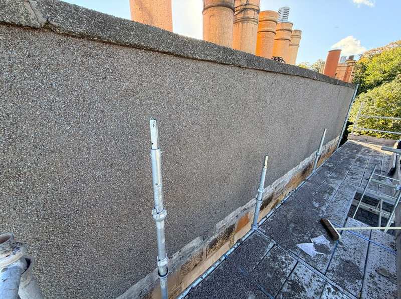 Chimney stack finished in new roughcast, seen along its length from roof scaffolding, with clay pots along the top