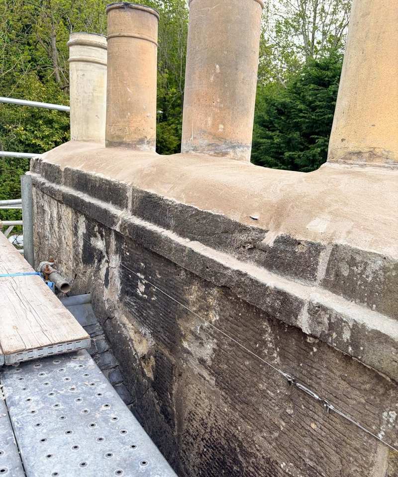 Blackened sandstone chimney stack with four clay pots, seen from a scaffold platform