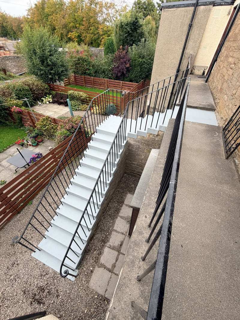 Finished concrete stair and landing seen from above, with new grey treads and iron railings