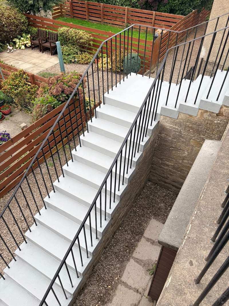 Refurbished grey concrete stair seen from the top landing, running down to a garden