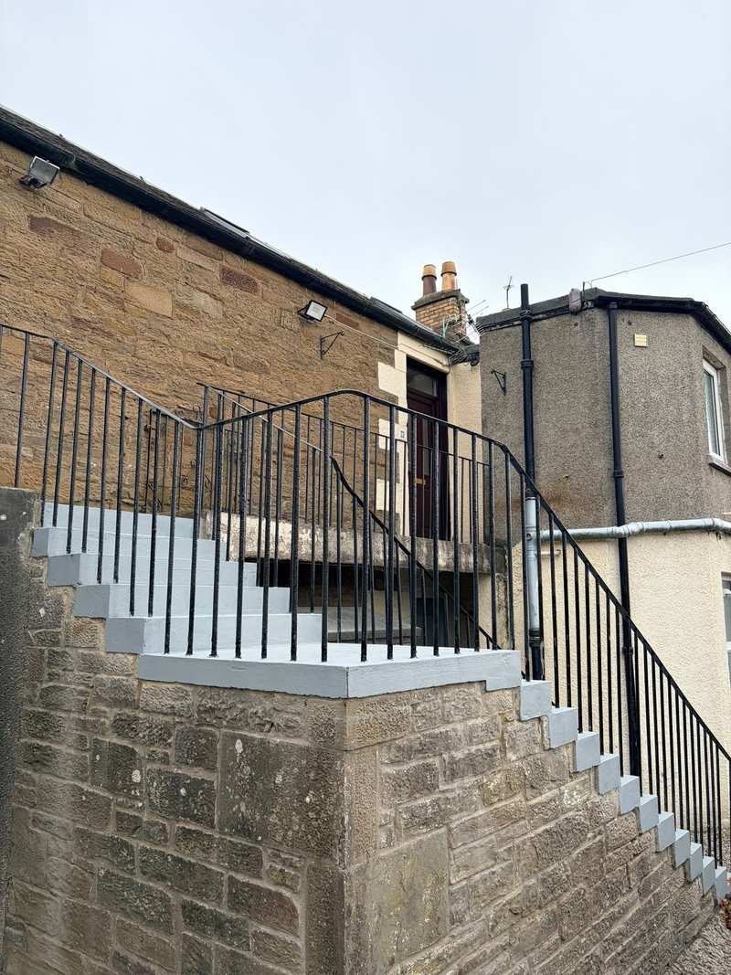 New concrete landing edge and top steps sitting on a sandstone wall, with iron railings above
