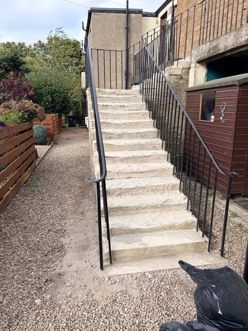 Worn and stained concrete external stair with black iron railings, seen from the bottom step
