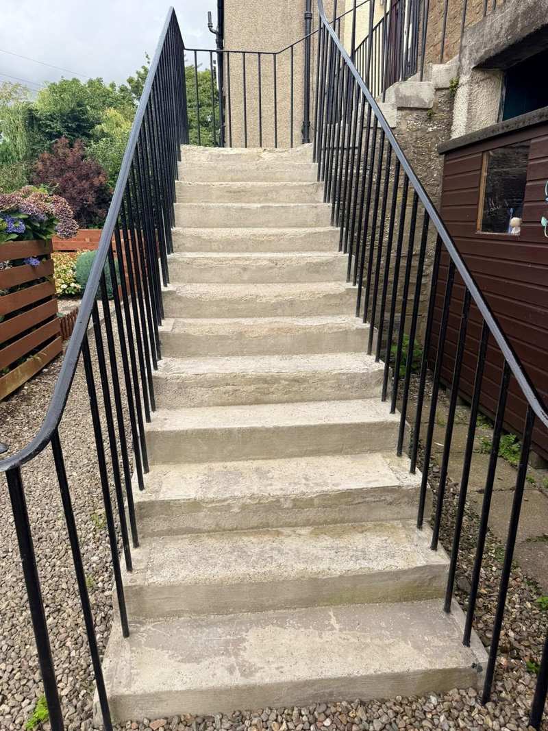 Close view of worn concrete steps with rounded, eroded nosings between iron railings