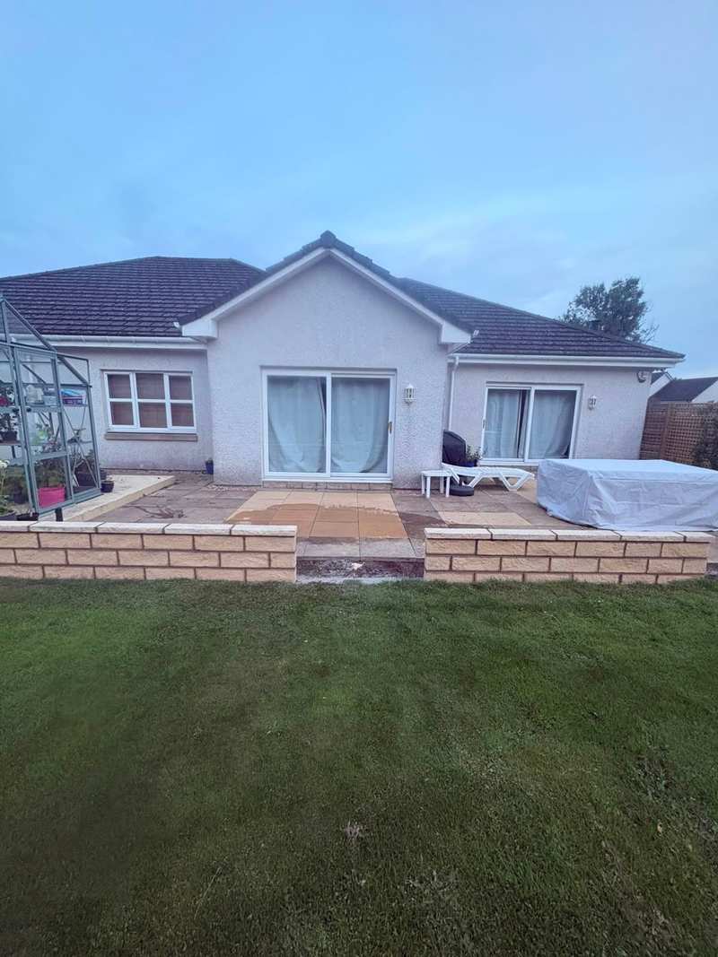 Two runs of low buff masonry garden wall with coping stones in front of a patio at the back of a bungalow