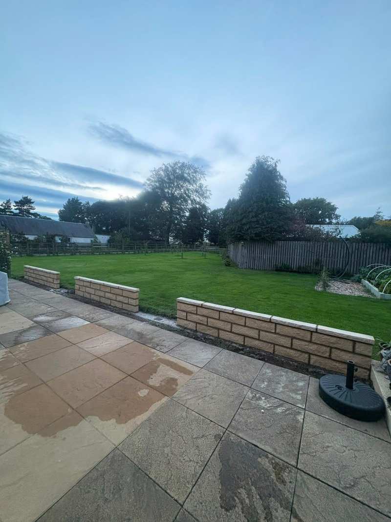 Low buff masonry garden walls with coping stones seen from a paved patio, with a lawn beyond