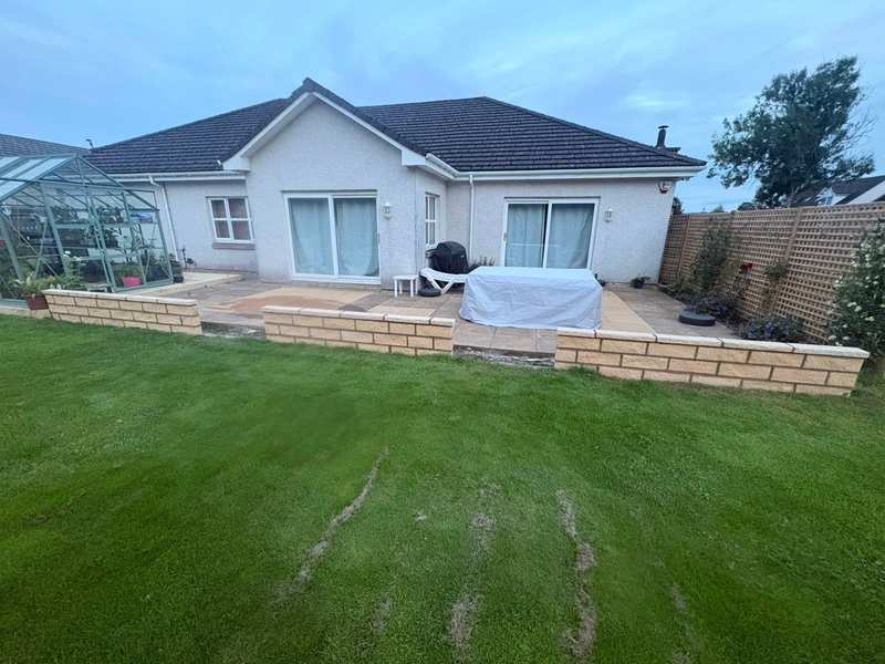 New low buff masonry garden walls with coping stones between a paved patio and a lawn behind a bungalow
