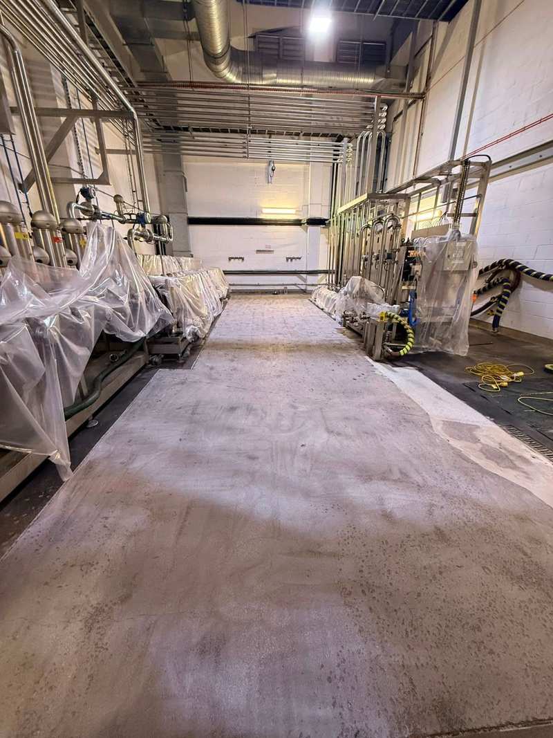 Long view of a prepared concrete floor in a plant room, with protected equipment along both walls