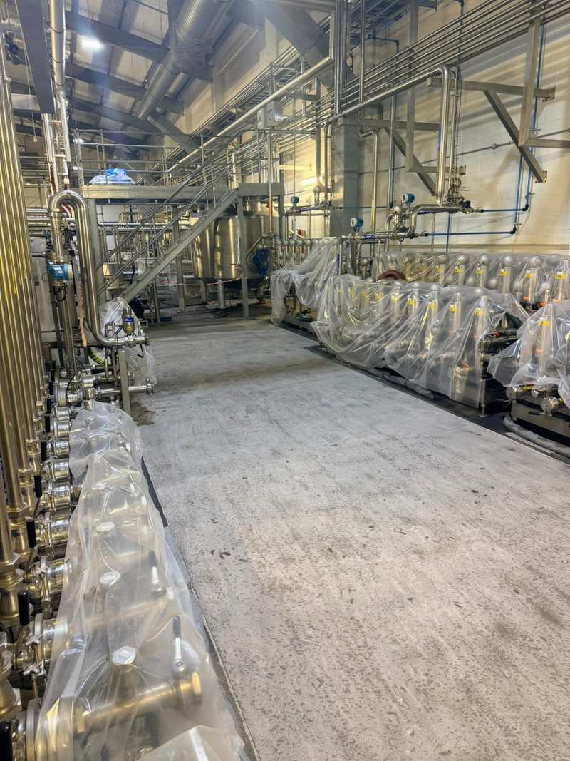 Ground concrete floor in an aisle between stainless pipework, with plant sheeted in polythene before resin flooring