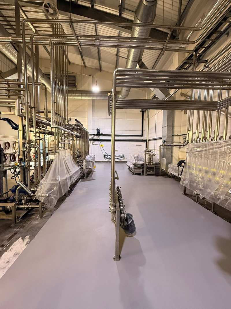 Grey resin floor between stainless steel pipe racks in a process plant, freshly finished