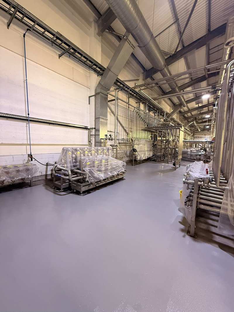 Finished grey resin floor running the length of a process plant hall, with stainless pipework and wrapped plant on both sides