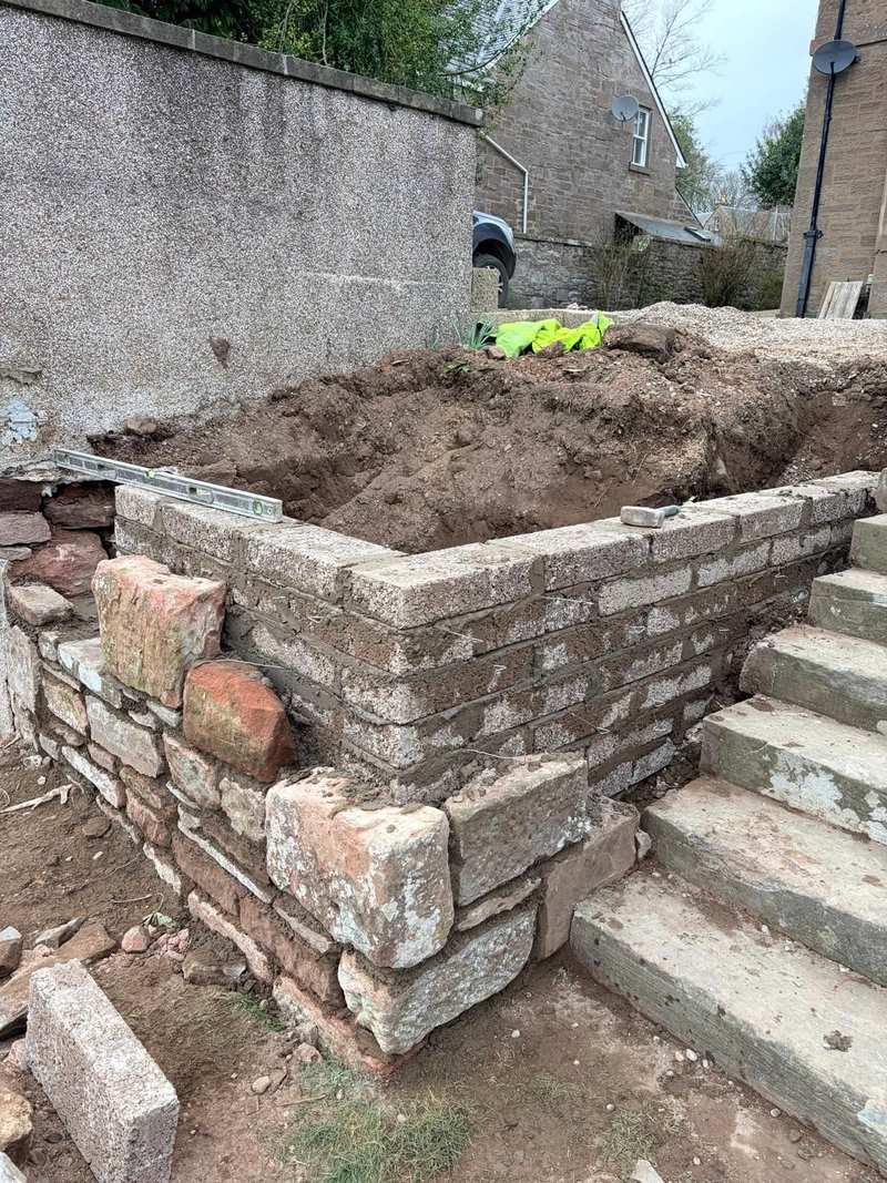 Stone boundary wall part rebuilt beside a flight of stone steps, with excavated ground behind