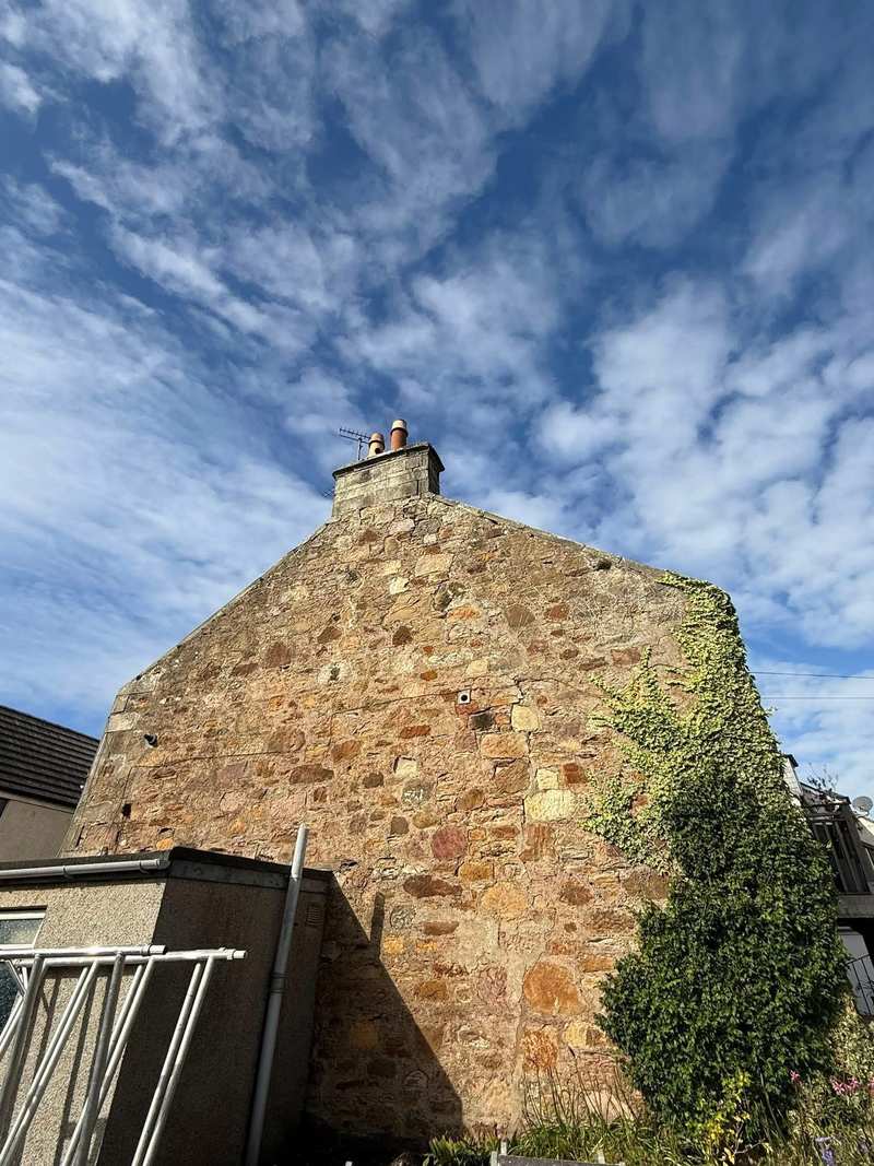 Rubble stone gable end with ivy growing over one side and open mortar joints