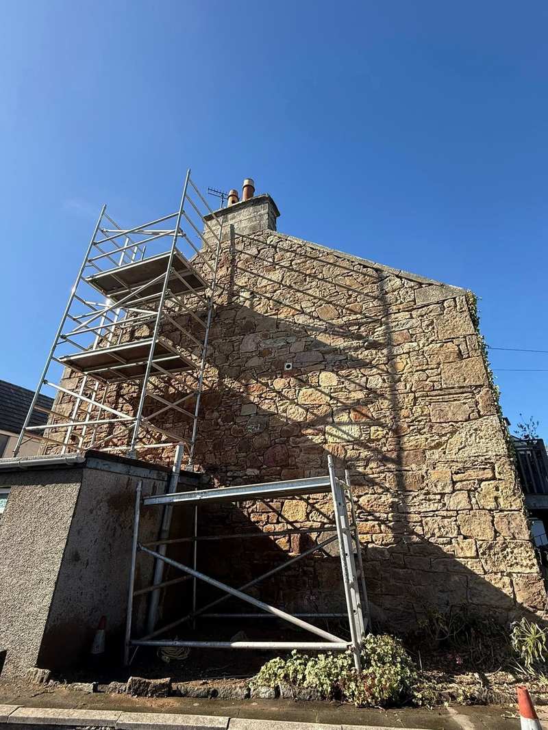 Tower scaffold erected against a stone gable end with the ivy cleared