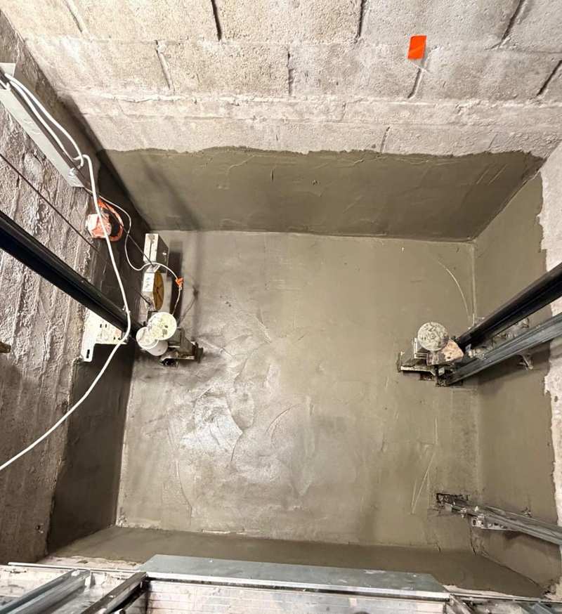 Finished lift shaft pit with cured cementitious waterproofing across the floor and up the walls, lift rails and buffers in place