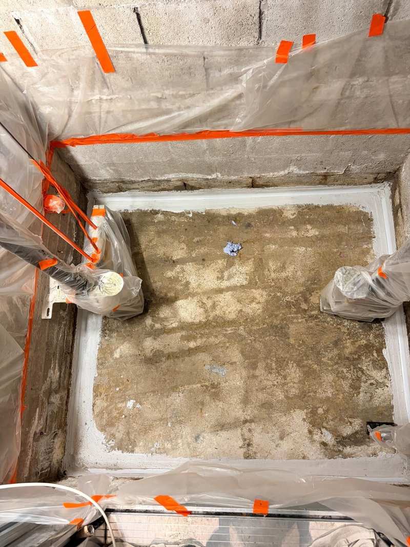 Concrete lift shaft pit prepared for waterproofing, with cement fillets at the floor to wall joints and lift equipment masked